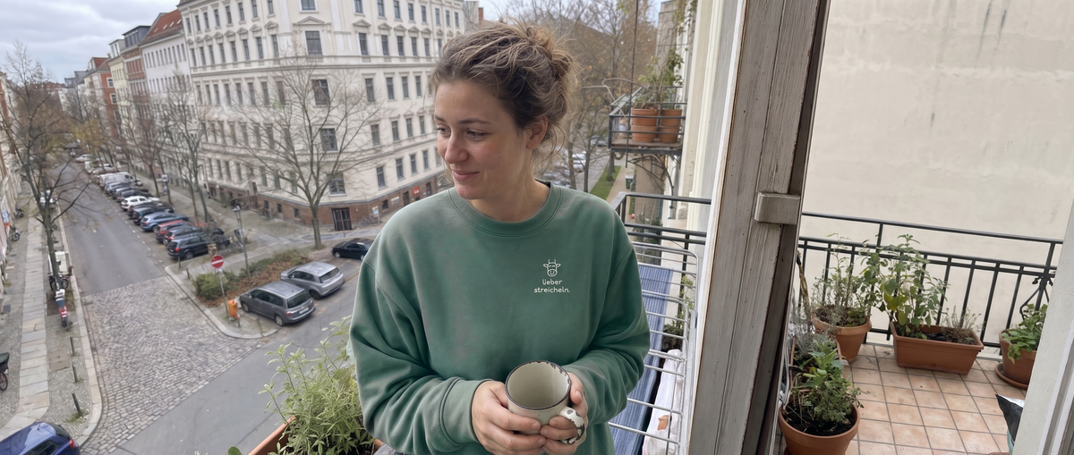 Frau im salbeigrünen Sweater „lieber streicheln.“ auf dem Balkon (KI-generiert)